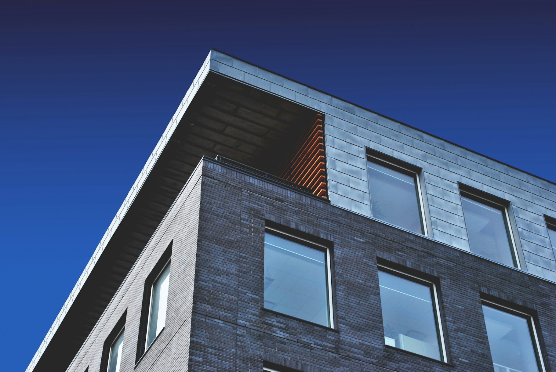 Fassadenreinigung Moderne Gebäude mit schrägem Dach und großen Fenstern vor blauem Himmel.